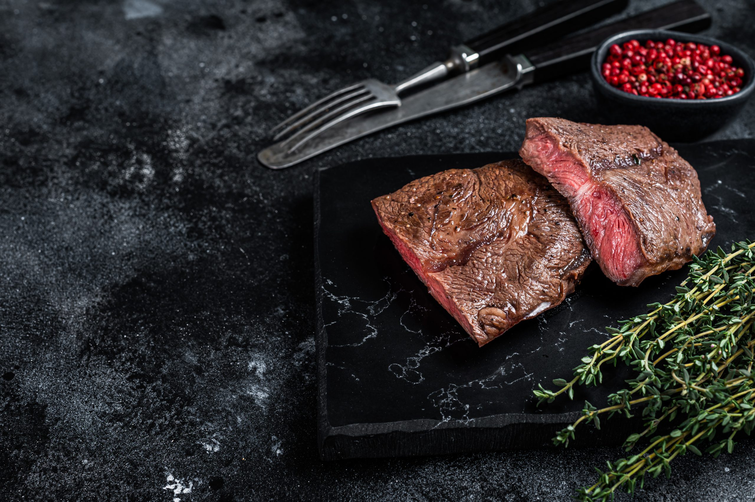Grilled Top Blade or flat iron roast beef meat steaks on marble board. Black background. Top View. Copy space.
